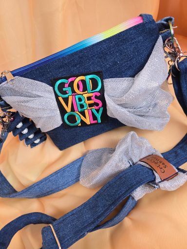 Blaues Täschchen mit buntem Schriftzug "GOD VIBES ONLY" und grauen Schleifen.