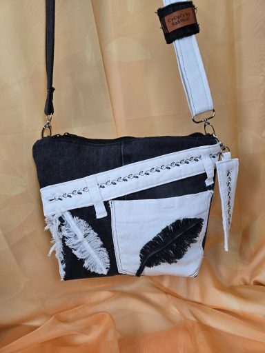 Schultertasche aus schwarzem und weißem Material mit Federmotiven.