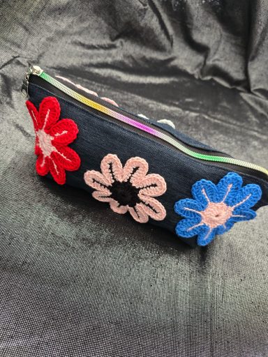 Schwarze Tasche mit bunten Blumenapplikationen in Rot, Rosa und Blau.
