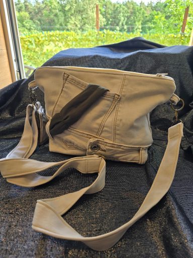 Beige Umhängetasche mit länglichem Tragegurt und schwarzem Akzent.