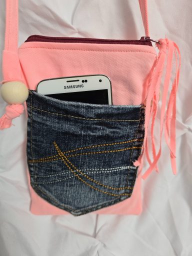 Rosa Umhängetasche mit einer Jeans-Tasche, die ein Smartphone hält.