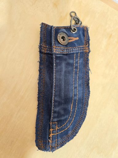 Jeansstoff-Tasche mit Metallknopf und orangefarbenen Nähten.