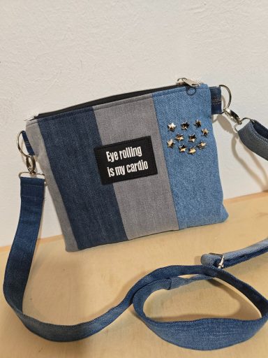 Kleine Umhängetasche aus Jeansstoff in Blau- und Grautönen mit Applikationen.