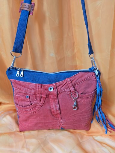 Tasche in Rot und Blau mit Quaste und Reißverschluss auf orangefarbenem Hintergrund.
