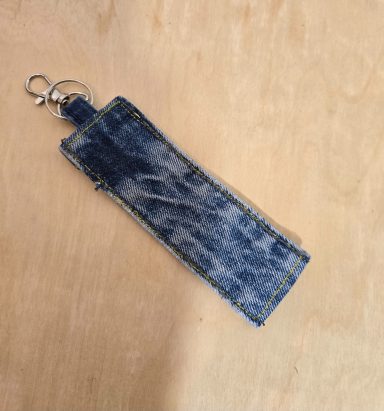 Blauer Schlüsselanhänger aus Jeansstoff mit einem metallischen Karabinerhaken.