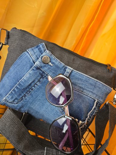 Schwarze Tasche mit Jeansstoff und einer Sonnenbrille darauf.