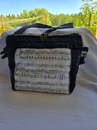 Schwarze Tasche mit einem Muster aus Notenblättern und einem Reißverschluss.
