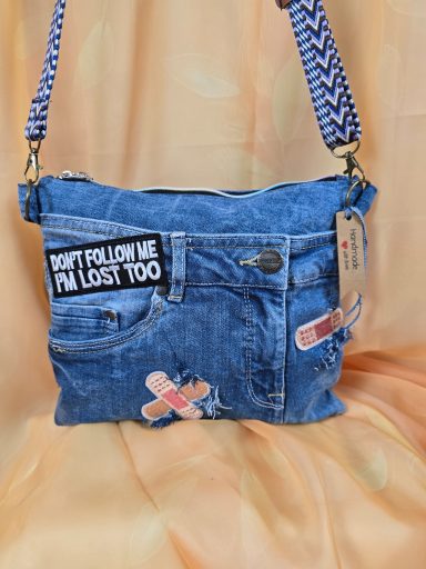 Tasche aus Jeansstoff mit bunten Pflastern und Schriftzug auf der Vorderseite.