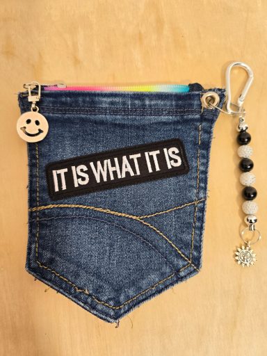 Kleine Jeans-Tasche mit dem Schriftzug „IT IS WHAT IT IS“ und einem Smiley-Anhänger.