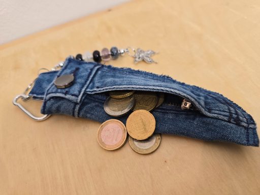 Eine kleine, offene Denim-Tasche mit Münzen darin, auf einem Holztisch.