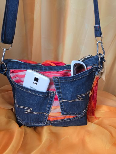 Tasche aus Jeansstoff mit buntem Innenfutter und zwei Handys in den Außenfächern.