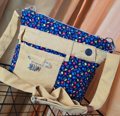 Beige Tasche mit buntem Muster, mehreren Fächern und verstellbarem Tragegurt.