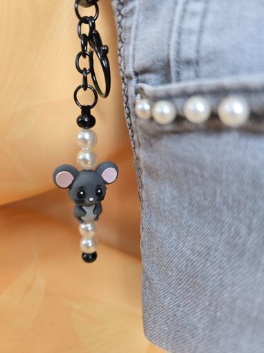 Graues Kleidungsstück mit einem Anhänger eines Mausmotivs aus Perlen.
