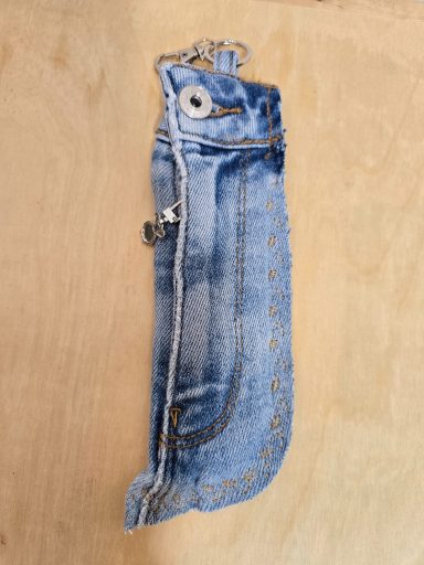 Jeans-Case mit Knopf und Reißverschluss auf hellem Holzuntergrund.