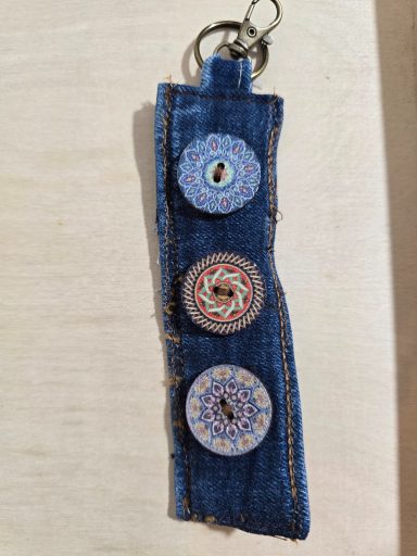 Drei bunte, runde Knöpfe auf einem Streifen aus Jeansstoff.