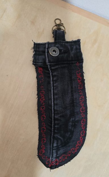 Schwarze Stofftasche mit roter Stickerei und schwarzem Knopfverschluss.