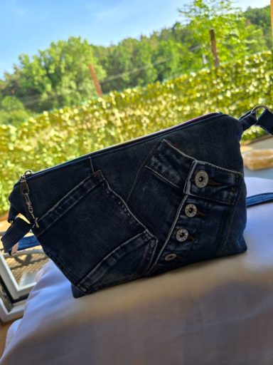Braune Handtasche aus Denim mit verschiedenen aufgenähten Taschen und Knöpfen.