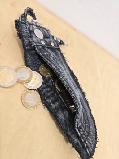Graue Geldbörse aus Denim mit Münzen darauf liegend.