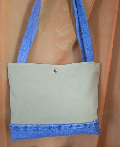Beige Handtasche mit blauen Trägern und einer kleinen dekorativen Knopfdetails.
