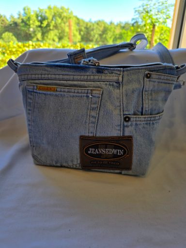 Tasche aus Jeansstoff mit mehreren Taschen und braunem Lederlabel.