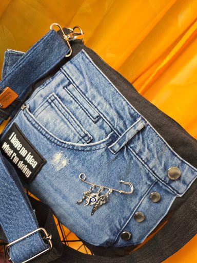 Tasche aus Denim mit auffälliger Vorderseite und schwarzem Schultergurt.