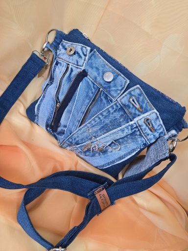 Tasche aus Jeansstoff mit Reißverschlüssen in verschiedenen Größen auf orangefarbenem Untergrund.