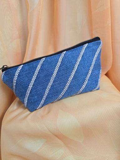 Blaue Kosmetiktasche mit weißen Streifen auf einem hellen, weichen Hintergrund.